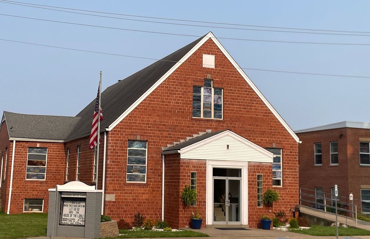 The red-brick Mid-America Baptist Church building on 2nd Street, with an American flag and the church sign out front