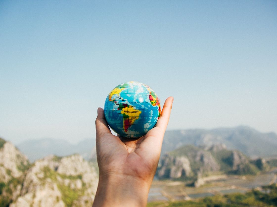 A hand holding a small globe against a mountain landscape