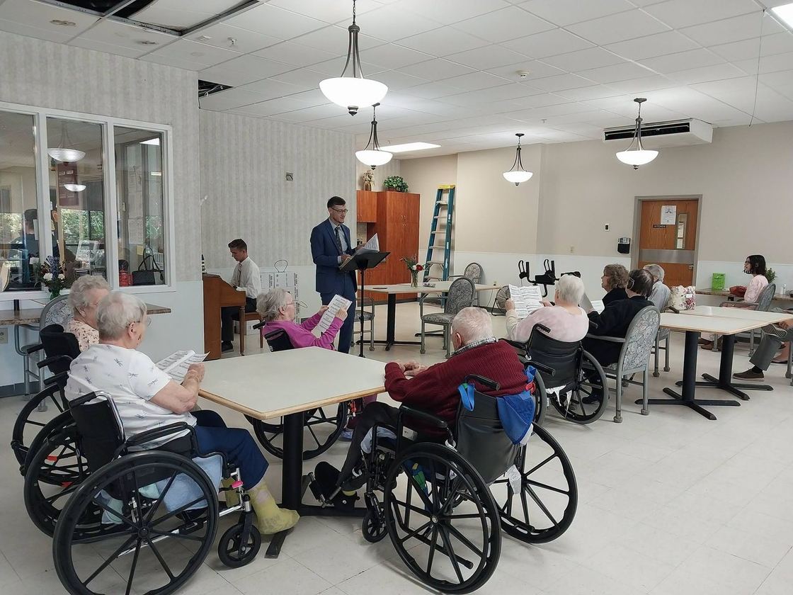 A church member preaching to residents seated at tables in the Elsberry Health Care Center