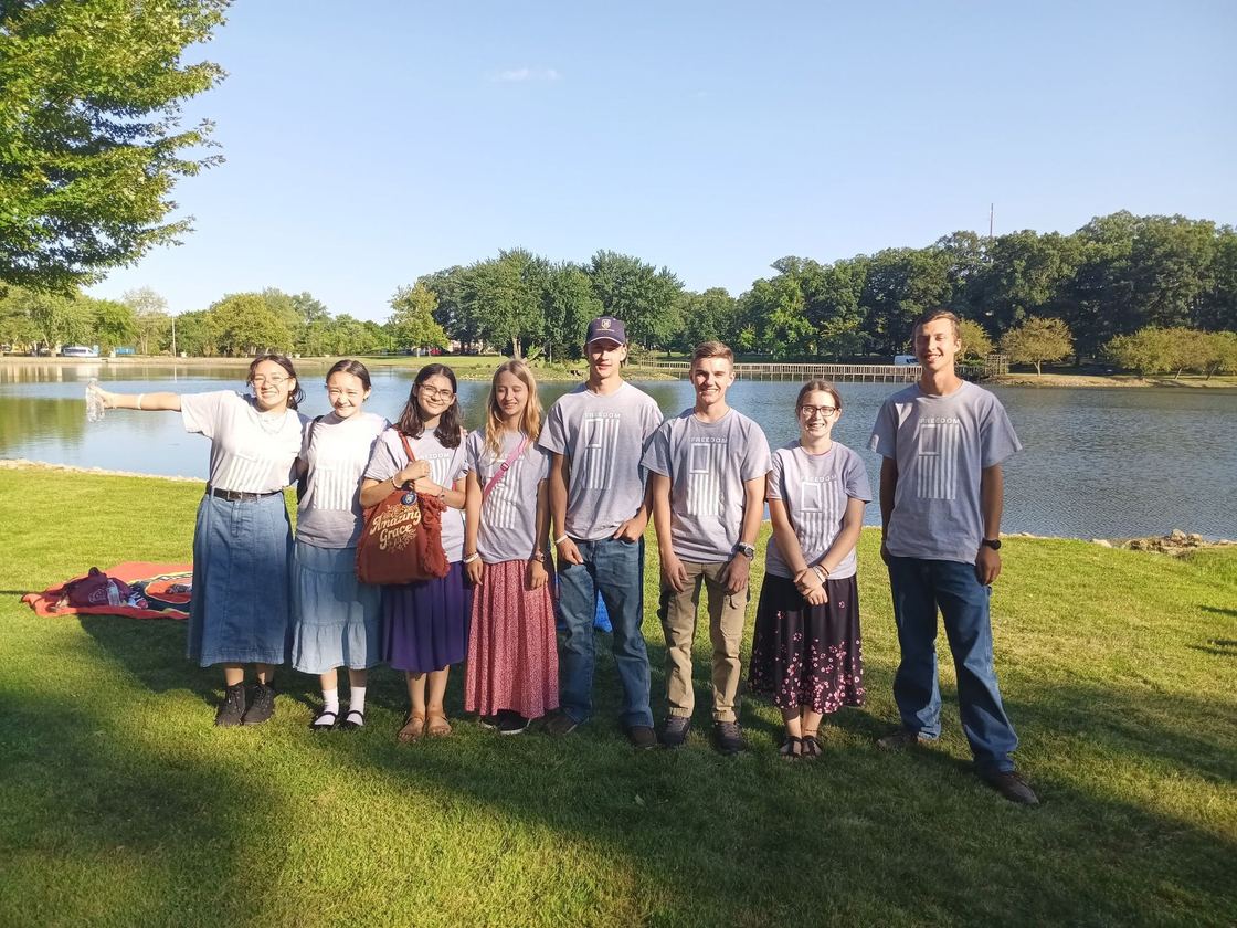 The church youth group standing together on the grass beside a lake