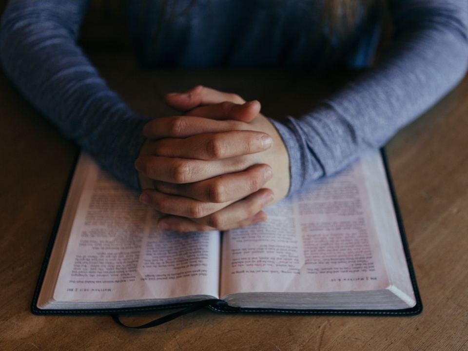 Hands folded in prayer on an open Bible