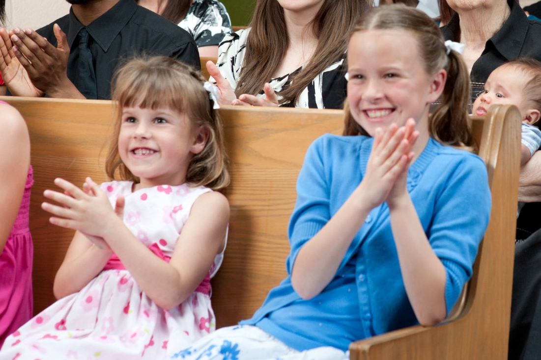 Two young girls smiling and clapping in a church pew