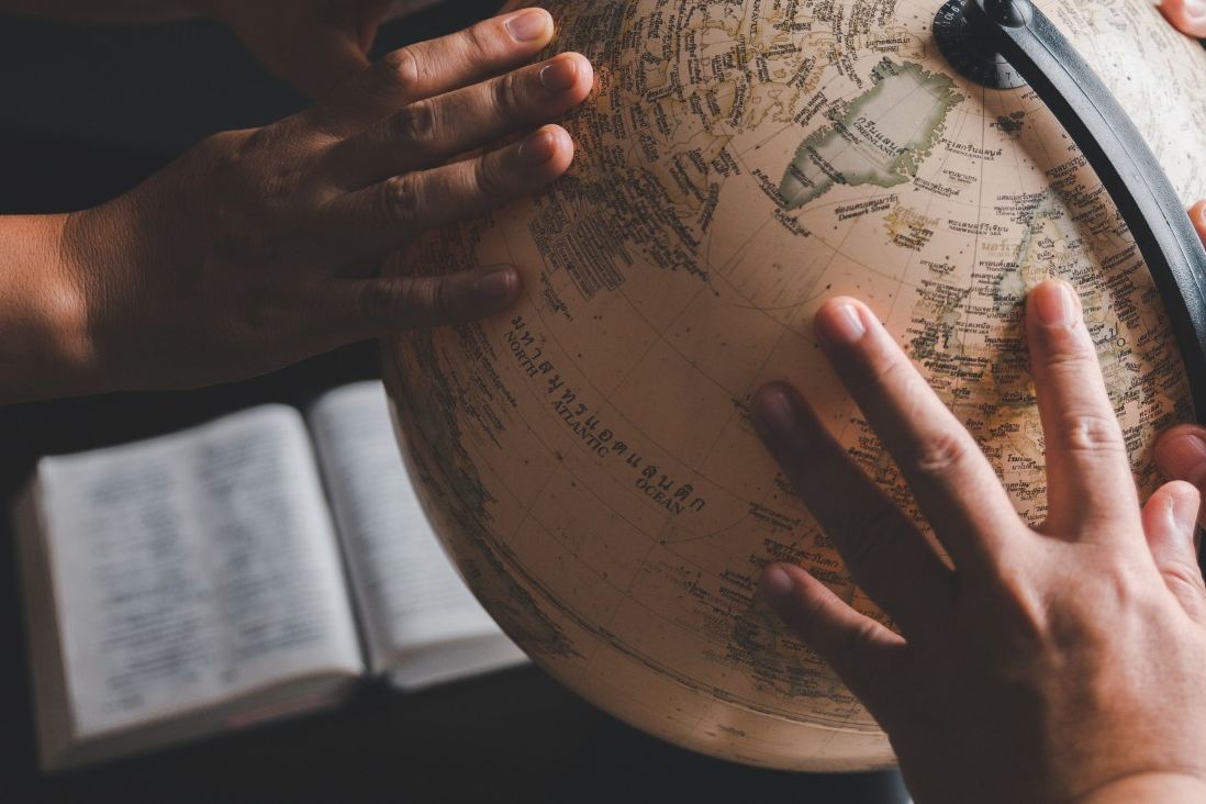 Hands resting on a globe beside an open Bible
